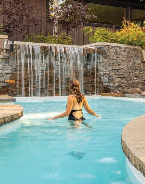 Outdoor Nordic spa pool with waterfall, featuring a person enjoying a thermal bath experience in Blue Mountain, Ontario.