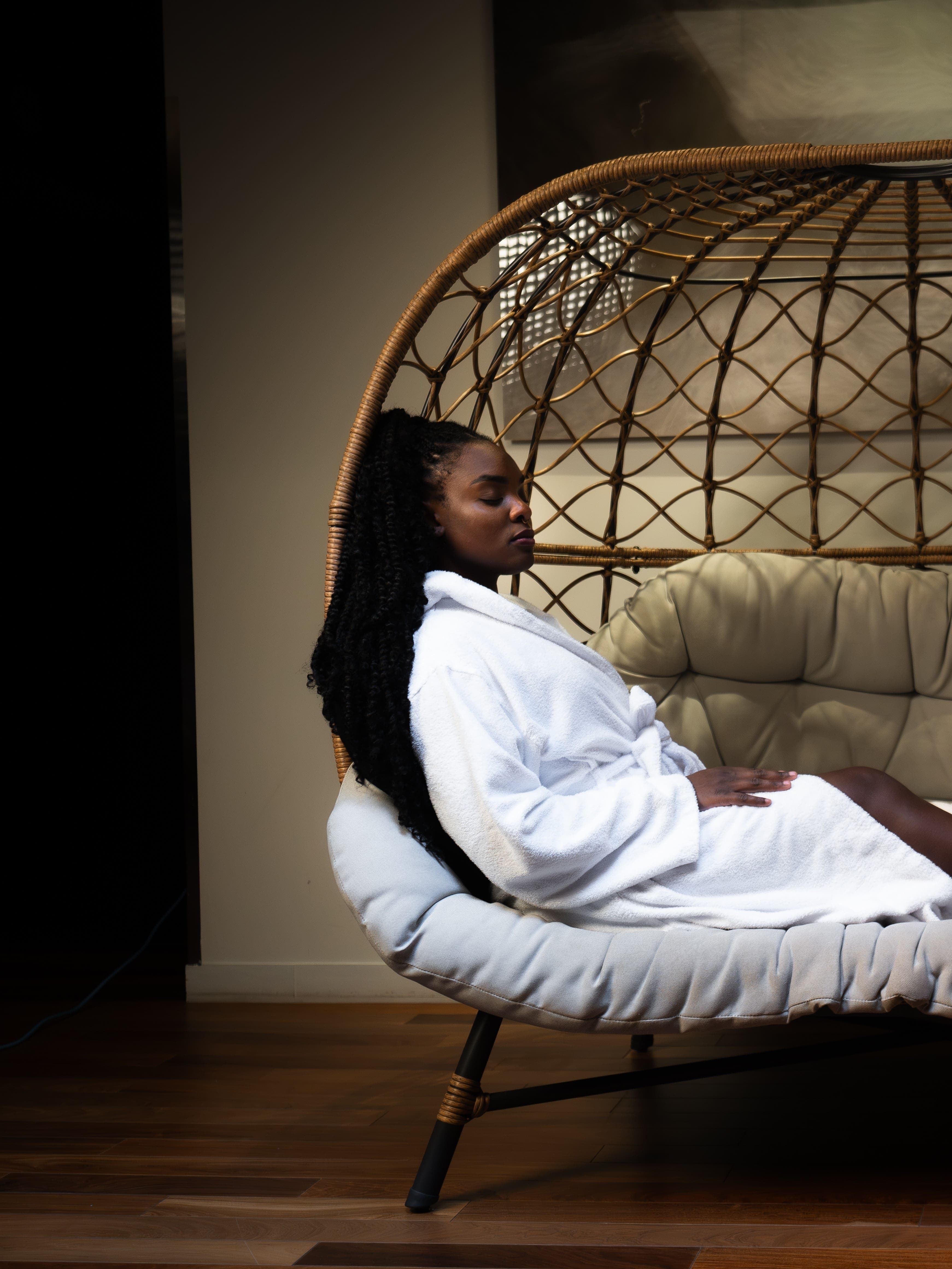 A woman in white bathrobes relaxing on a large wicker chair in a spa setting.
