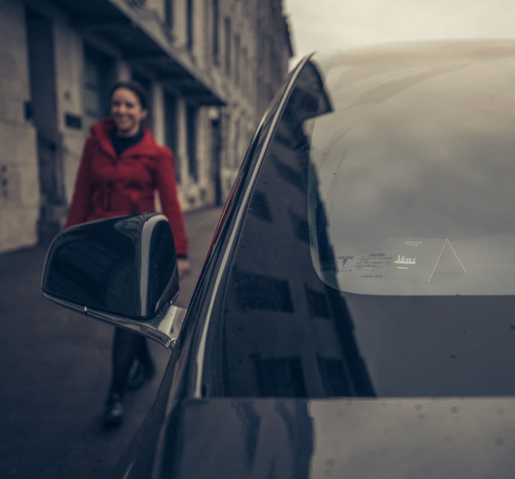 A person wearing a red coat uses the valet service on a cobblestone street lined with historic buildings, in front of the Scandinave Spa Vieux Montréal entrance.