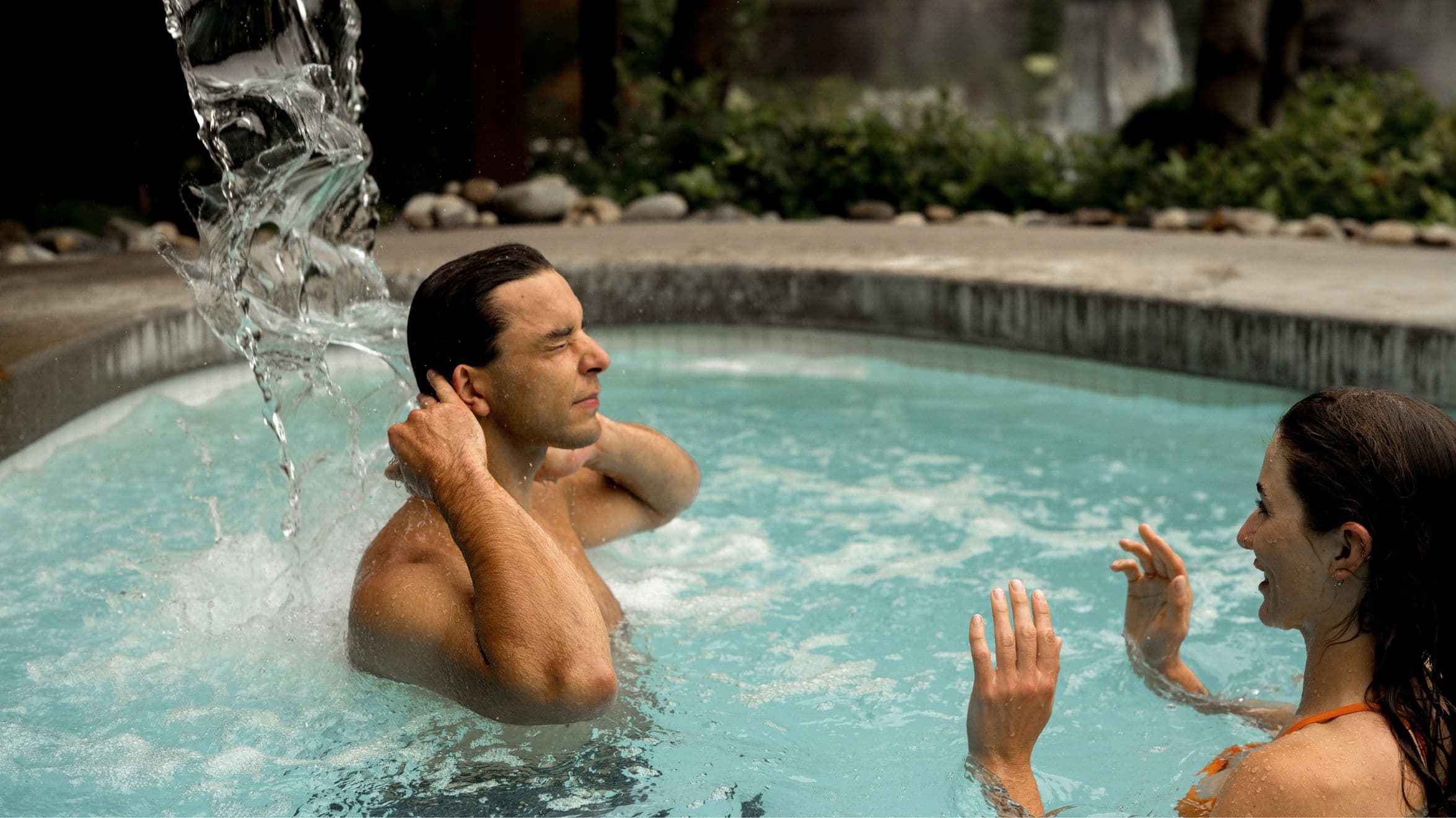 Couple in a cold plunge pool, with the man standing under the Nordic waterfall at Scandinave Spa.