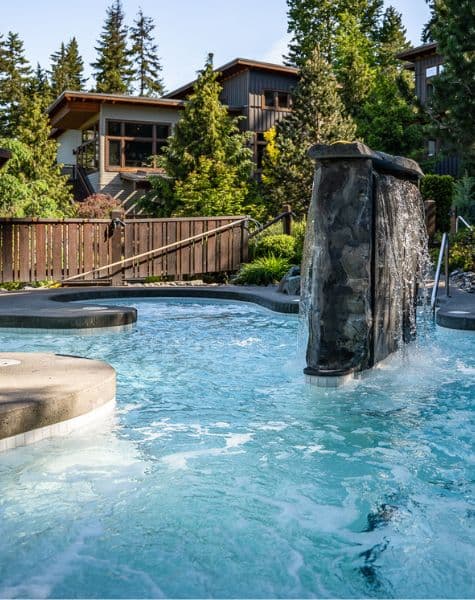 Outdoor hot pool at Scandinave Spa Whistler featuring a stone fountain with water cascading into the pool.