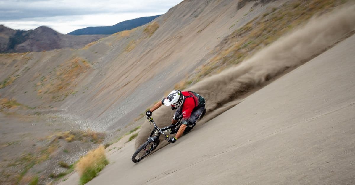 A mountain biker kicking up dust riding down a steep mountain slope