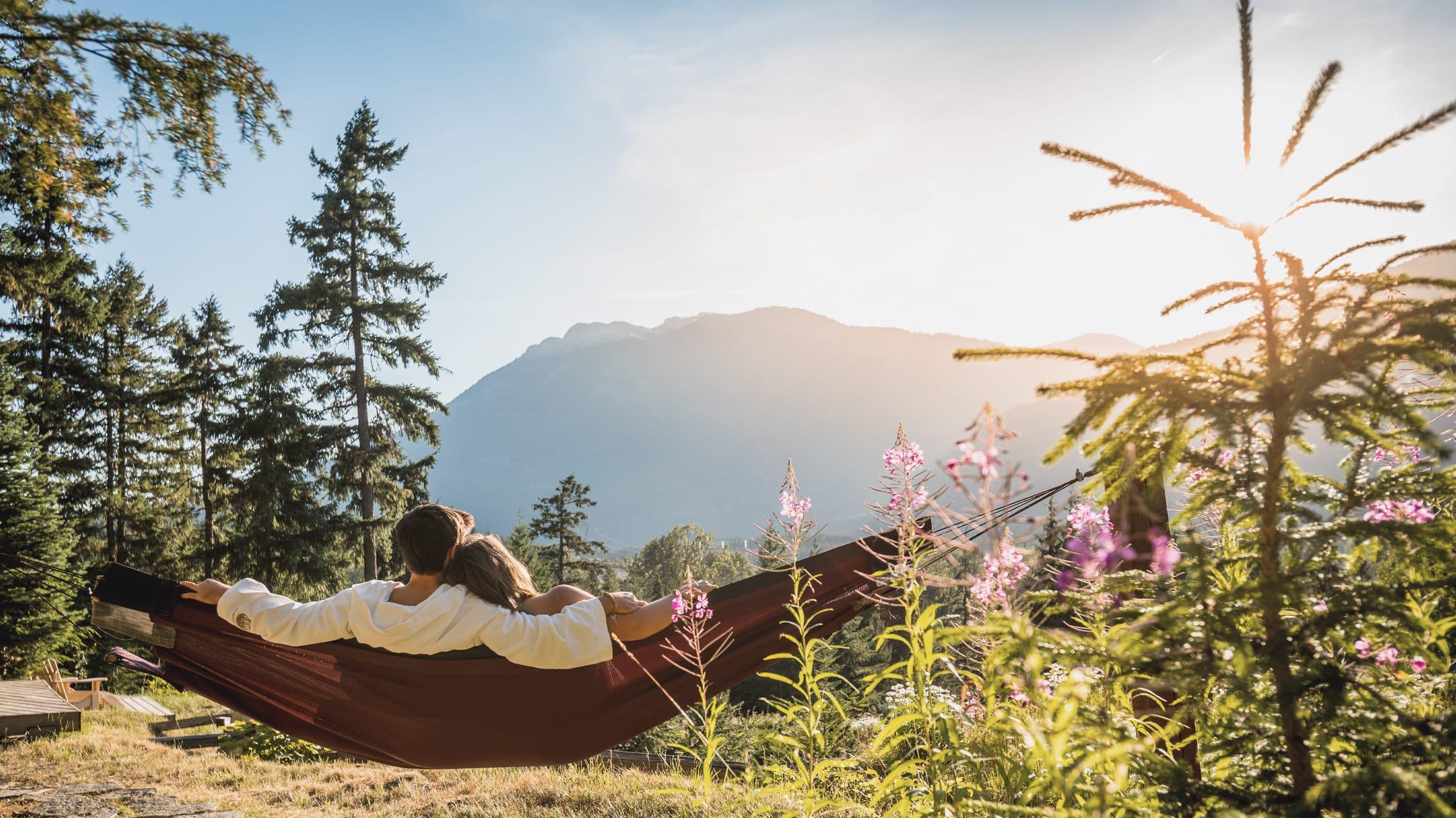 A couple relaxing at the Hammock Haven at Scandinave Spa Whistler and taking in the majestic Coastal mountains view.
