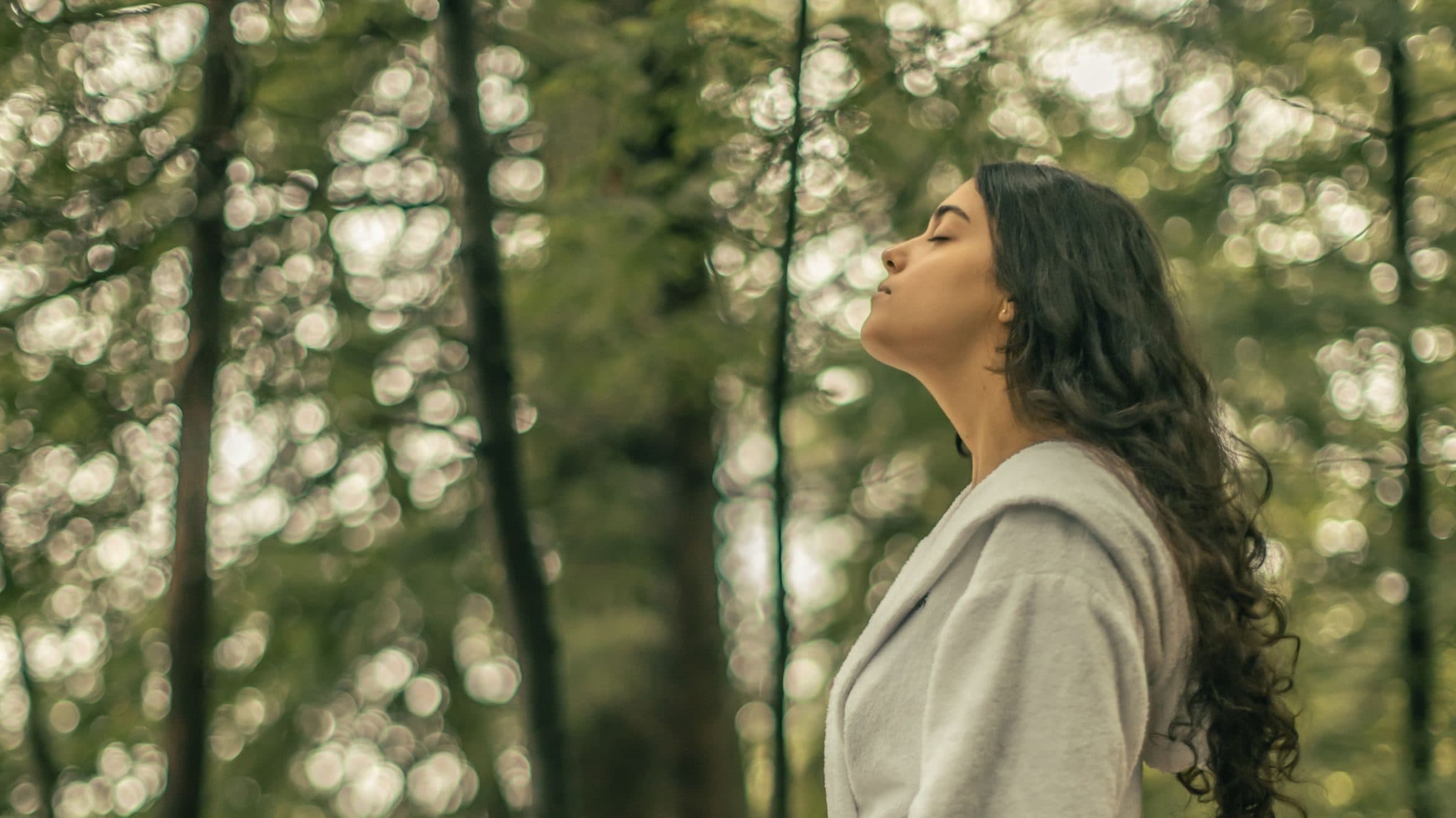 Personne se tenant paisiblement dans une forêt, profitant d’un moment de pleine présence et de déconnexion numérique en nature.