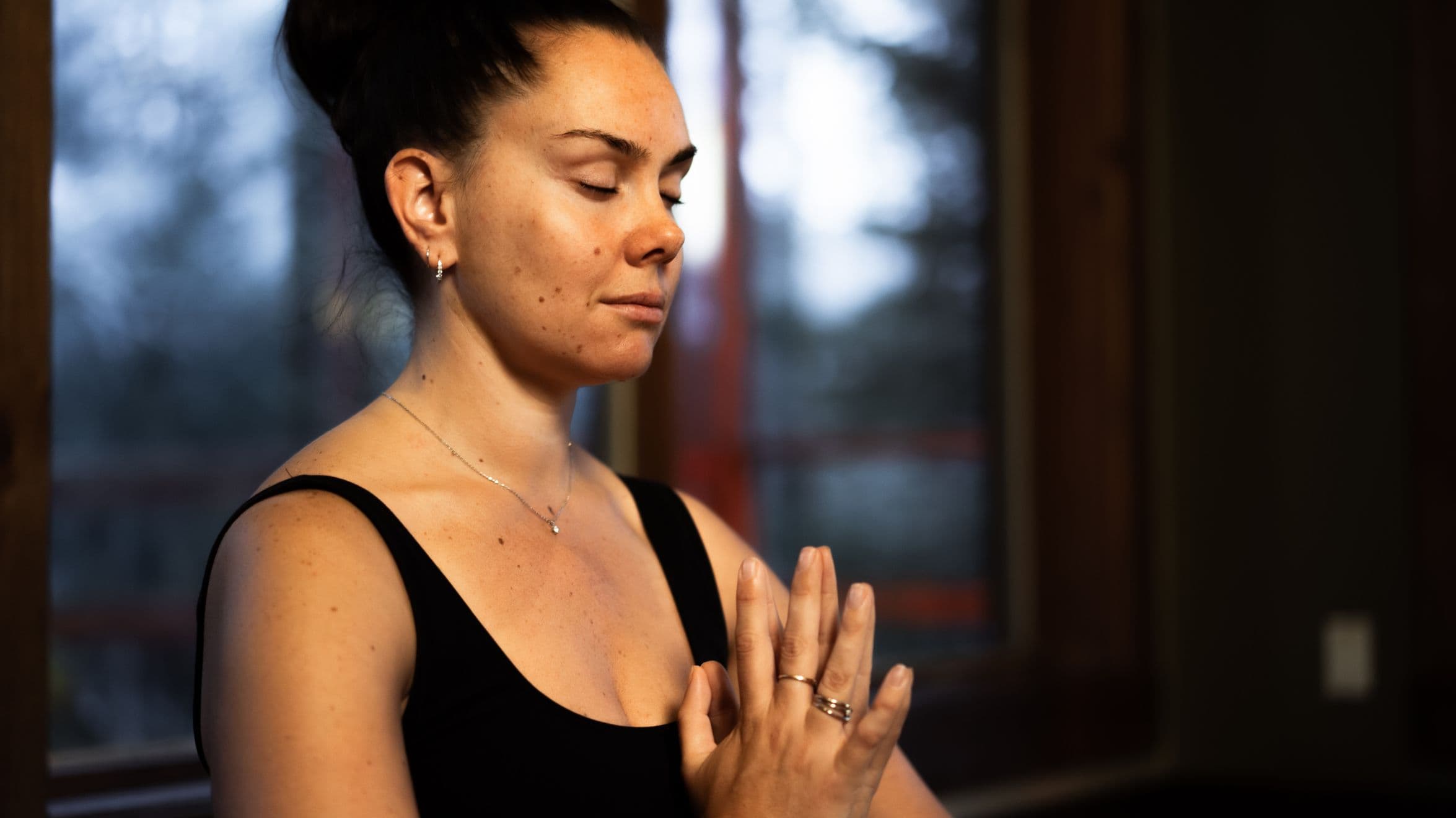 Personne en posture de méditation, les mains jointes au coeur, dans un espace intérieur calme.