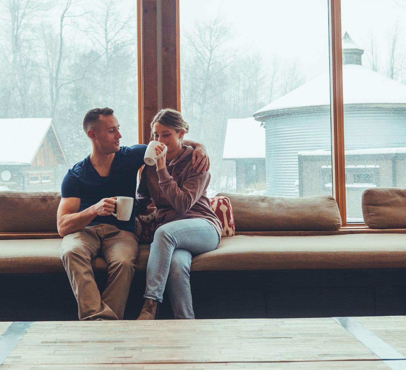 Couple sitting together in the spa’s cozy bistro lounge, sipping warm drinks while enjoying views of the snowy outdoor spa landscape.