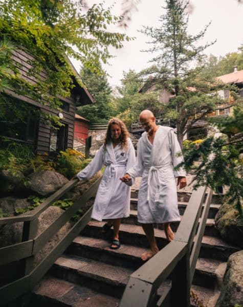 Couple walking hand in hand during summer at Scandinave Spa Mont-Tremblant, immersed in nature and tranquility.