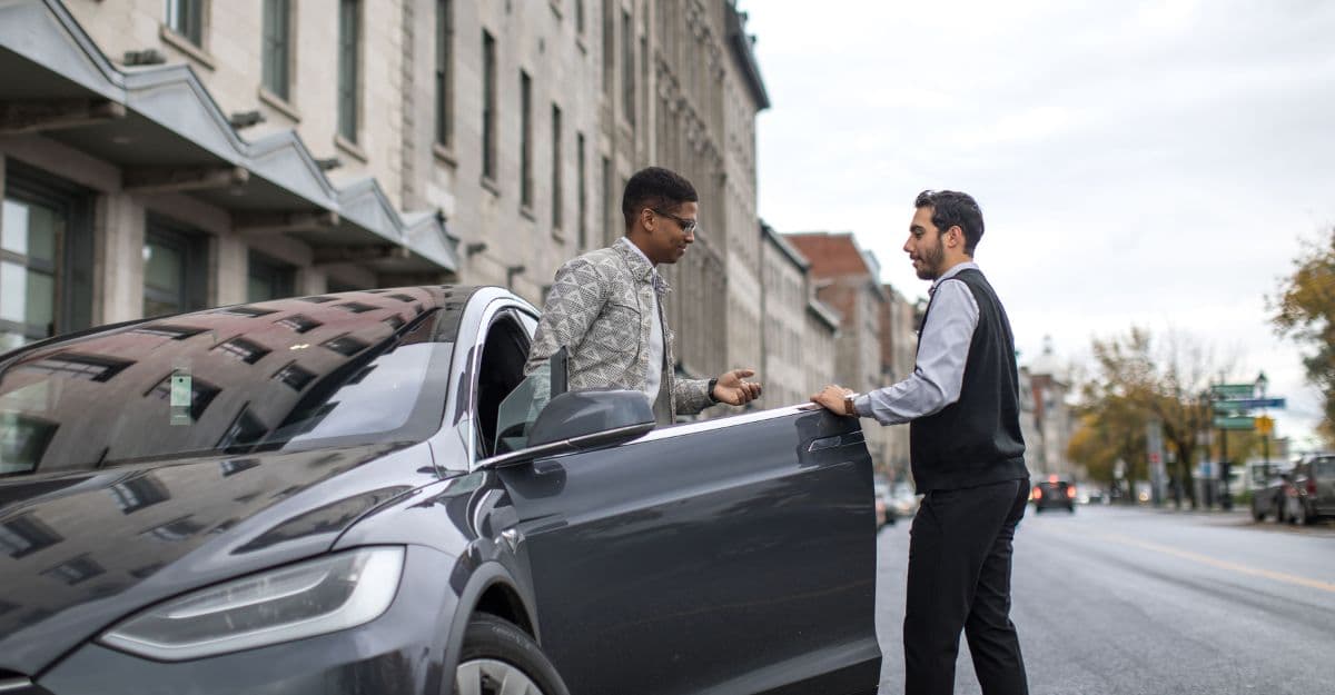 Deux personnes debout à côté d’une voiture garée dans une rue de la ville. Le conducteur remet les clés de la voiture au voiturier.
