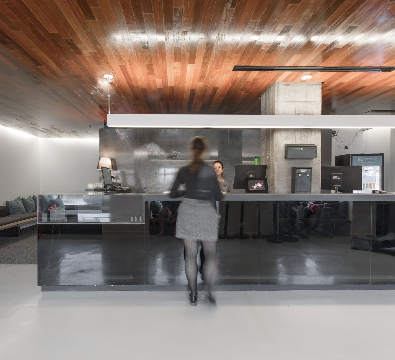 Une réception moderne avec un comptoir élégant, au design minimaliste. Une personne se tient devant le comptoir, face à un membre du personnel.