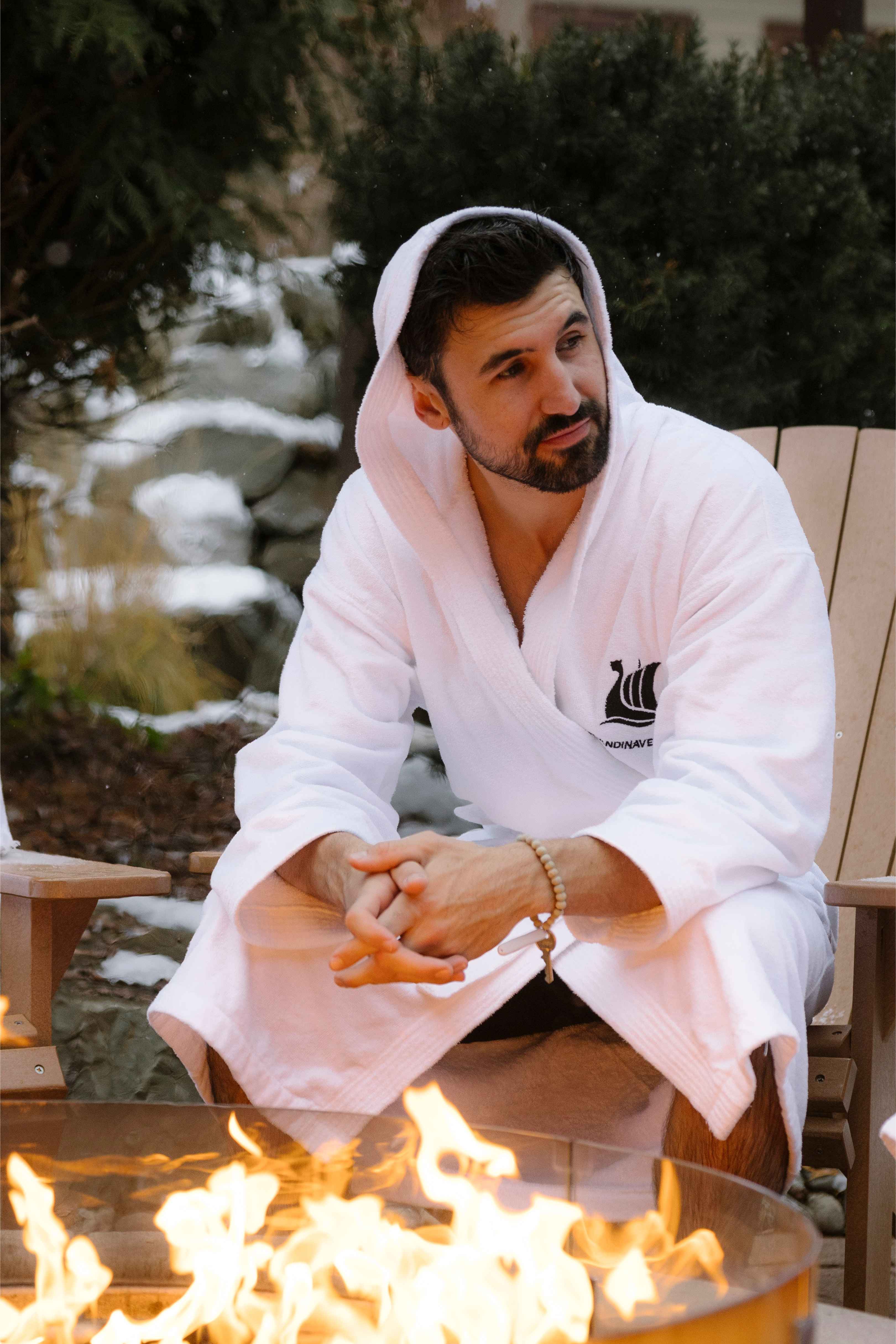 A man in a bathrobe relaxing next to the fire pit at Scandinave Spa Whistler, enjoying the warmth and tranquil atmosphere.