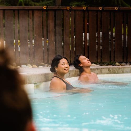 A woman and a man relaxing together in the hot pool at Scandinave Spa Whistler, surrounded by calm and warmth.