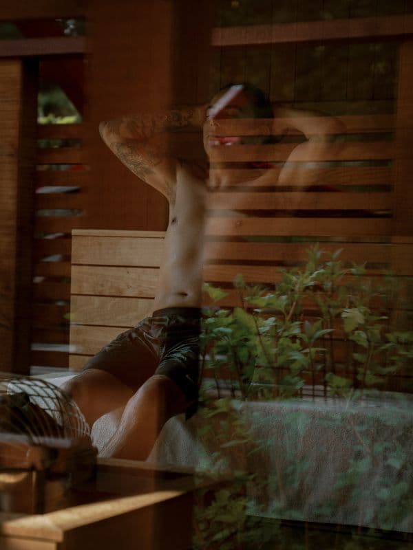 A man relaxing in the dry sauna at Scandinave Spa Whistler, viewed through the window, capturing the calm atmosphere inside.